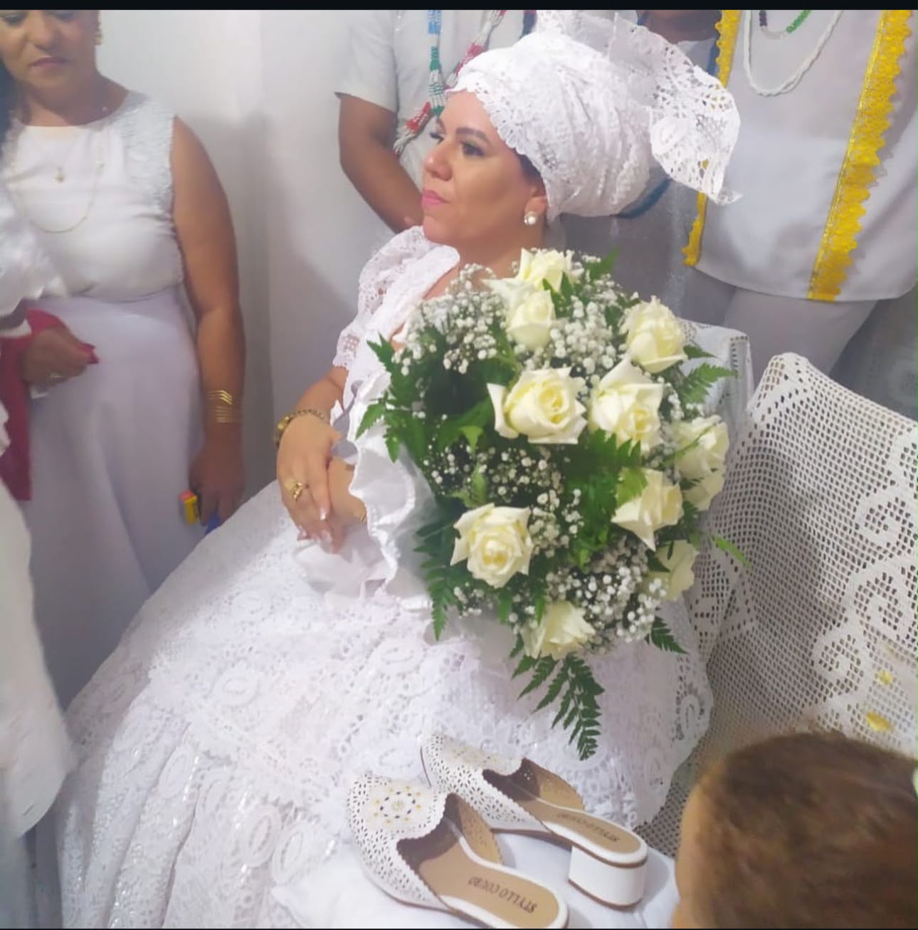 Mãe Débora sentada com um buquê de flores brancas na consagração